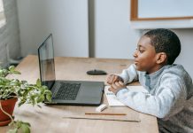 Uczeń szkoły podstawowej siedzi przy biurku i uczestniczy w zajęciach online na laptopie, obok leży zeszyt do notatek, ołówek i linijka. Chłopiec skupia się na ekranie podczas lekcji, co dobrze oddaje ideę kursów dla ósmoklasistów online Symposio przygotowujących do egzaminu ósmoklasisty – więcej informacji można znaleźć na stronie organizatora