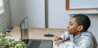 Uczeń szkoły podstawowej siedzi przy biurku i uczestniczy w zajęciach online na laptopie, obok leży zeszyt do notatek, ołówek i linijka. Chłopiec skupia się na ekranie podczas lekcji, co dobrze oddaje ideę kursów dla ósmoklasistów online Symposio przygotowujących do egzaminu ósmoklasisty – więcej informacji można znaleźć na stronie organizatora