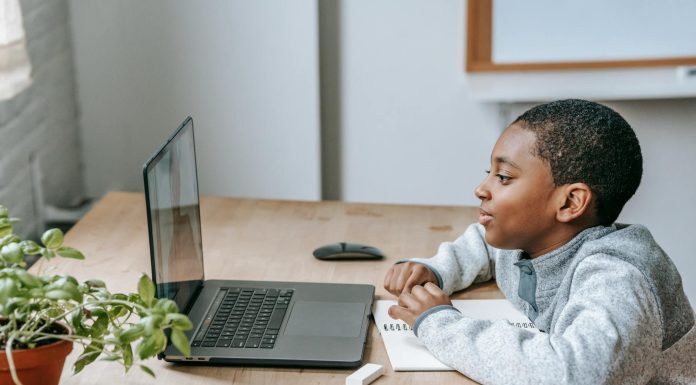 Uczeń szkoły podstawowej siedzi przy biurku i uczestniczy w zajęciach online na laptopie, obok leży zeszyt do notatek, ołówek i linijka. Chłopiec skupia się na ekranie podczas lekcji, co dobrze oddaje ideę kursów dla ósmoklasistów online Symposio przygotowujących do egzaminu ósmoklasisty – więcej informacji można znaleźć na stronie organizatora